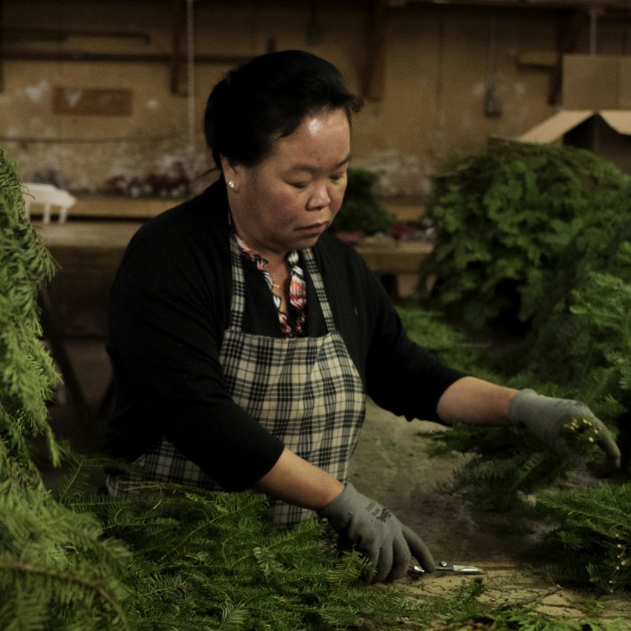 Woman in black sweater and apron building christmas wreaths.